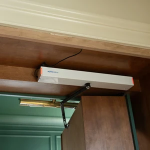 Automatic door opener mechanism mounted above a wooden door inside a cabinet.