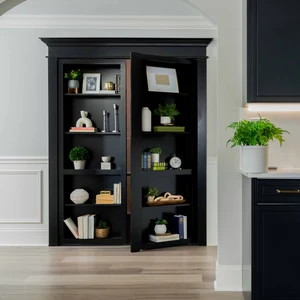 Black built-in bookcase doors open outward, revealing concealed storage in a modern kitchen area.