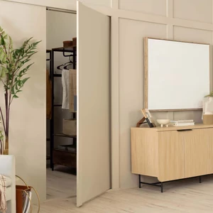 Flush wall panel door opens to a hidden walk-in closet, next to a light wood dresser and mirror.