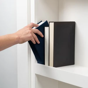 Hand removes a book from a shelf to access a hidden lock or release mechanism.