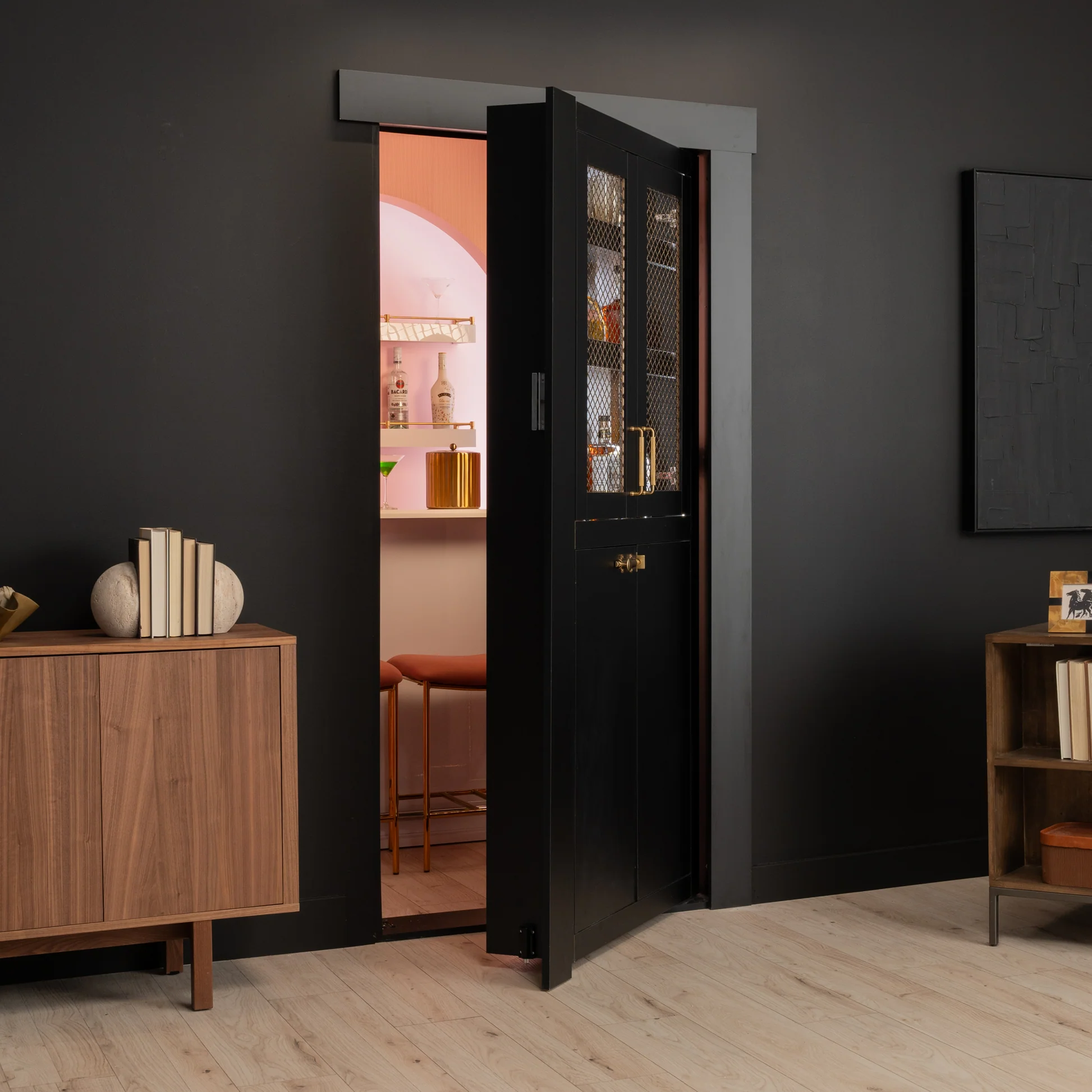 Murphy Door® sleek black hidden door with mesh panels revealing pink interior room with bar shelving and warm wood furnishings.
