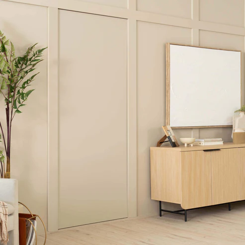 Murphy Door® concealed door in cream wall paneling beside light wood credenza with decorative fern plant and minimalist decor.